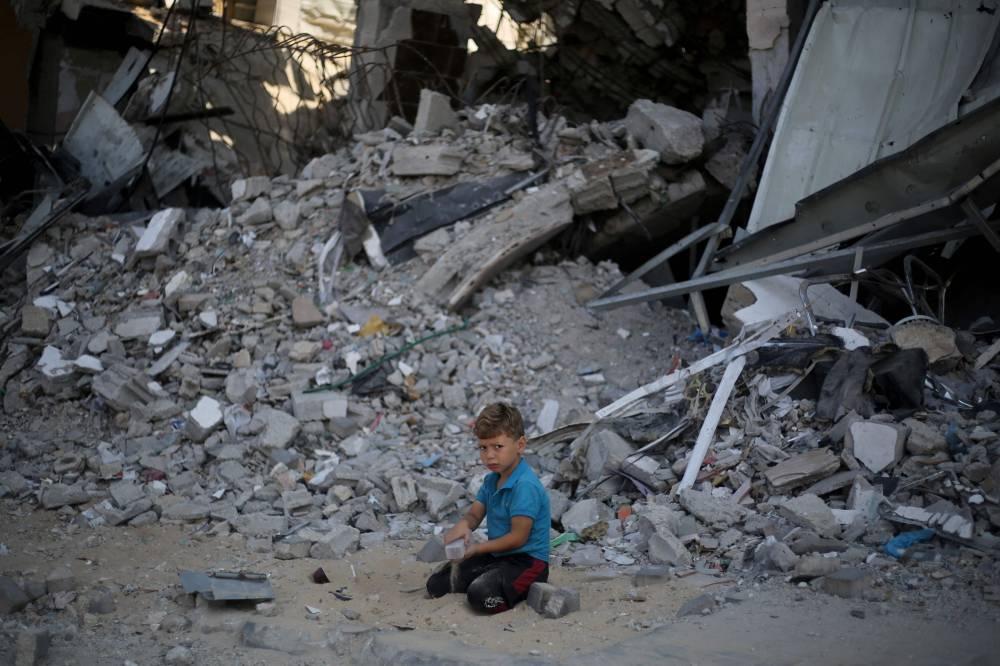 A Palestinian boy sits playing on the sand and rubble of a building destroyed in previous Israeli bombardment, in the Al-Bureij refugee camp in the central Gaza Strip, yesterday.