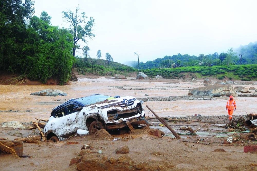 A rescuer walks past a damaged car at a landslide site after multiple landslides in the hills in Wayanad, Kerala, India, on Tuesday.
