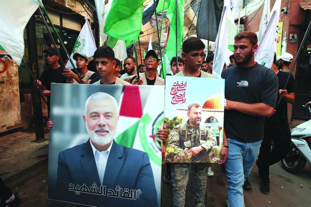 Palestinians carry pictures of Hamas' late deputy leader Saleh al-Arouri and leader Ismail Haniyeh, who was assassinated in Iran, during a march to condemn Haniyeh's killing, at Burj al-Barajneh Palestinian refugee camp in Beirut, Lebanon, yesterday.