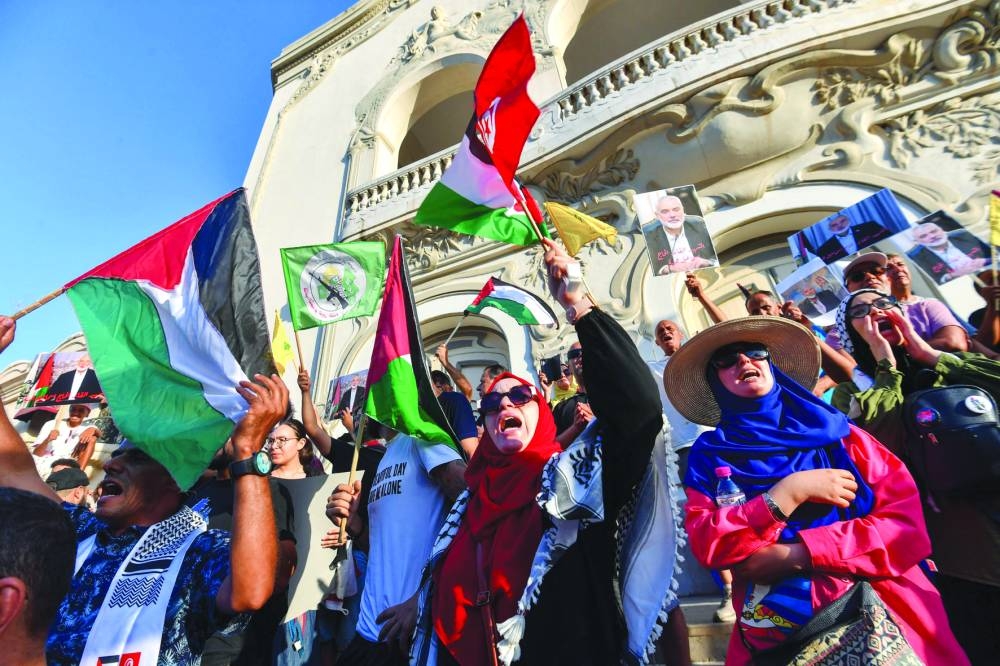 Tunisians wave Palestinian flags and hold portraits of slain Hamas leader Ismail Haniyeh during a protest in the capital Tunis, yesterday.