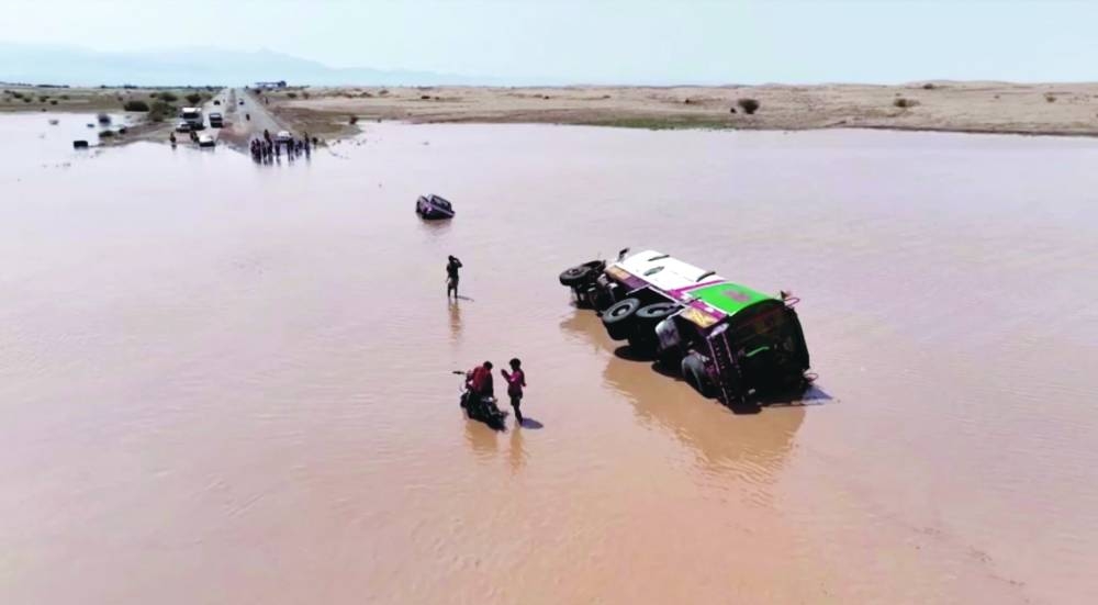 People standing next to a vehicle overturned on flood waters, in Hodeidah Province.