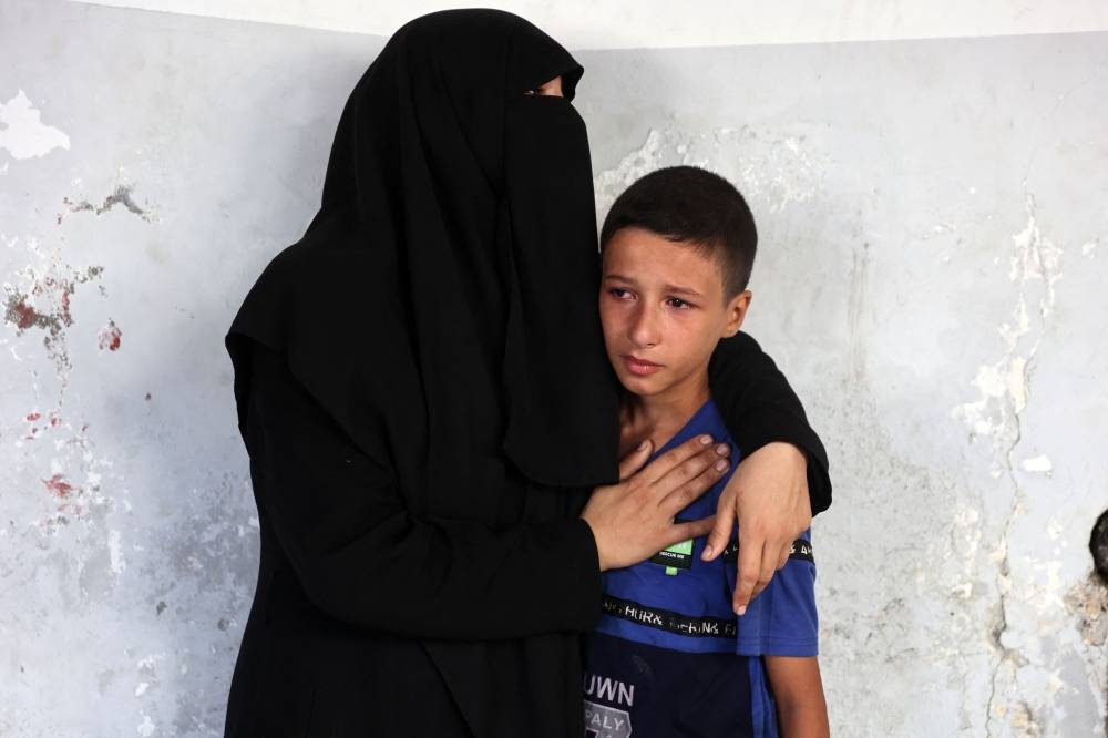 A young boy supported a women cries after identifying a member of his family among the dead at the al-Maamadani hospital, following an Israeli strike that killed more than 90 people on a school sheltering displaced Palestinians in Gaza City on  Saturday. AFP