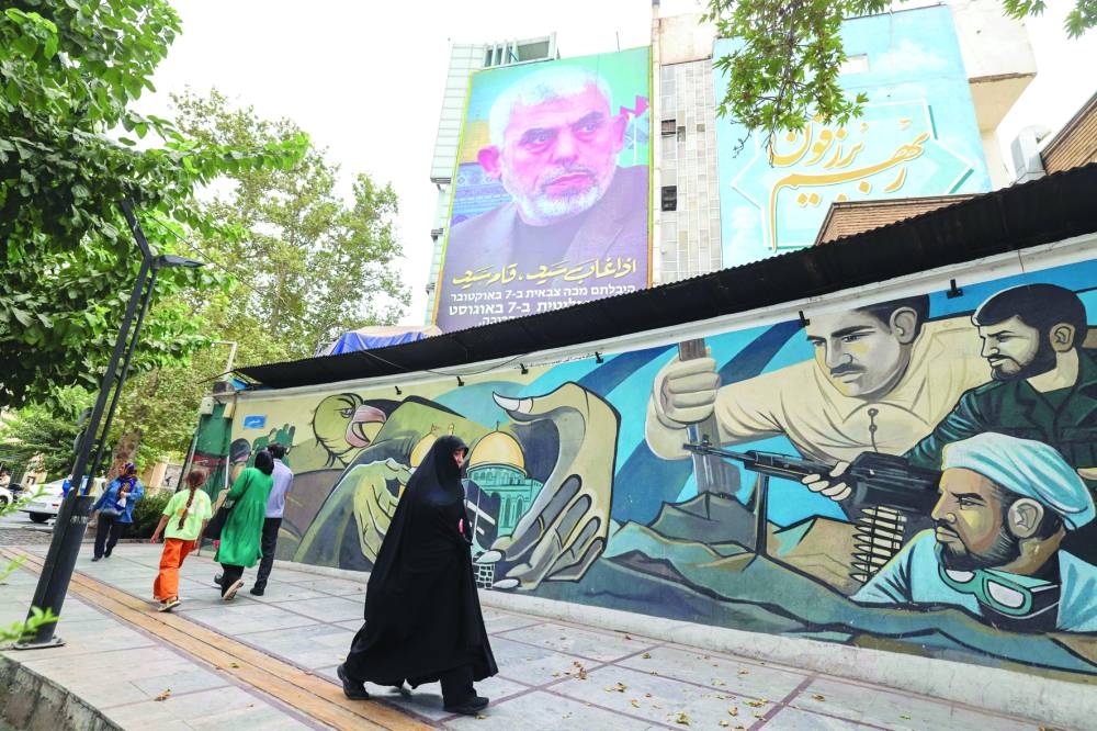 People walk past a billboard showing a portrait of newly appointed Hamas leader Yahya Sinwar (top) next to Palestine Square in the Tehran on Monday.