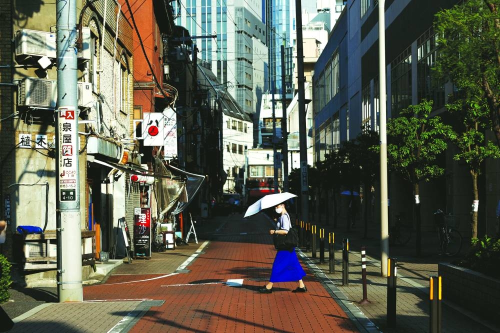 
A woman with an umbrella crosses a street during a hot summer day in Shimbashi, Tokyo. 