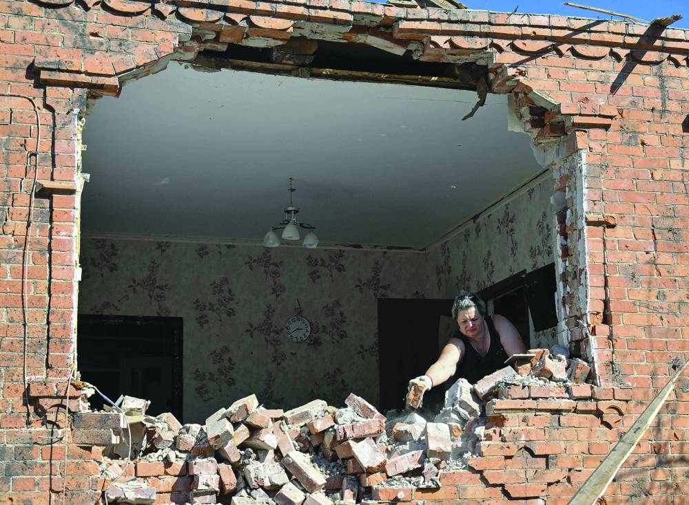 A woma clears debris around her house, which was heavily damaged following recent strikes in a village near Russian border in Sumy region. – AFP