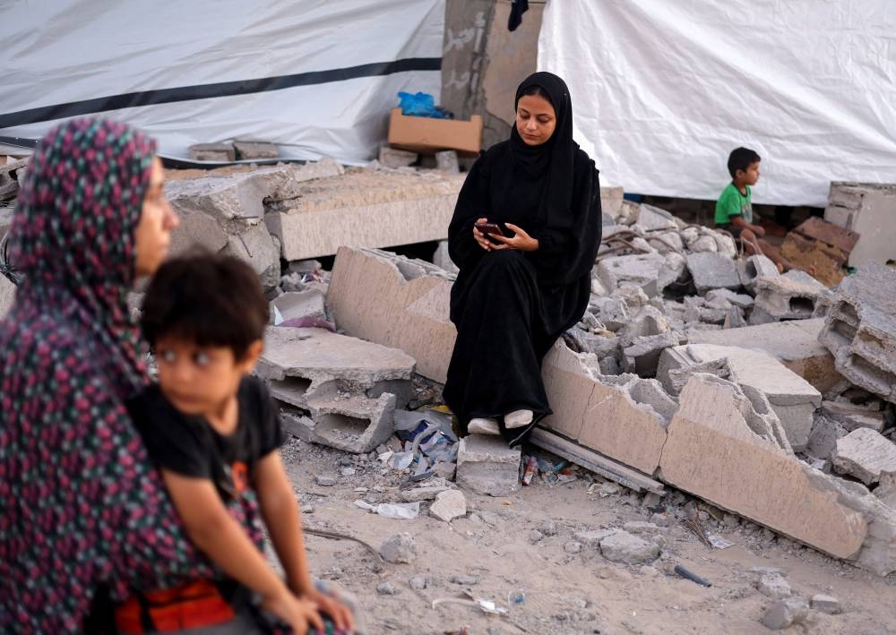 Shahed Abu Omar, a computer engineering student, sits on the rubble of a house studying online via her mobile phone, amid destruction and closure of schools and universities in Khan Younis in the southern Gaza Strip on Tuesday. REUTERS