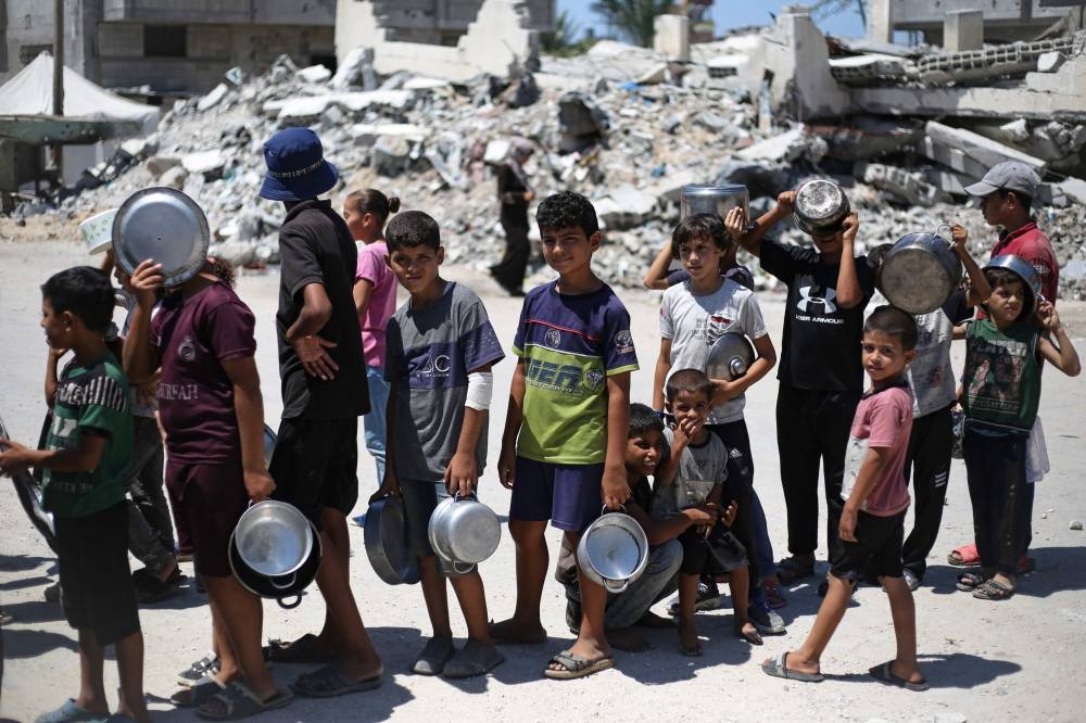 Palestinian children queue to receive a meal during food distribution in Bureij refugee camp central of Gaza Strip on Wednesday. AFP