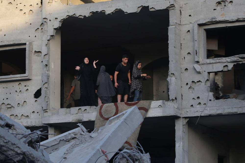 Palestinians stand on balcony of a damaged flat in the vicinity of a building shortly after it was levelled by Israeli bombing in the Nuseirat refugee camp in the central Gaza Strip on Thursday. AFP