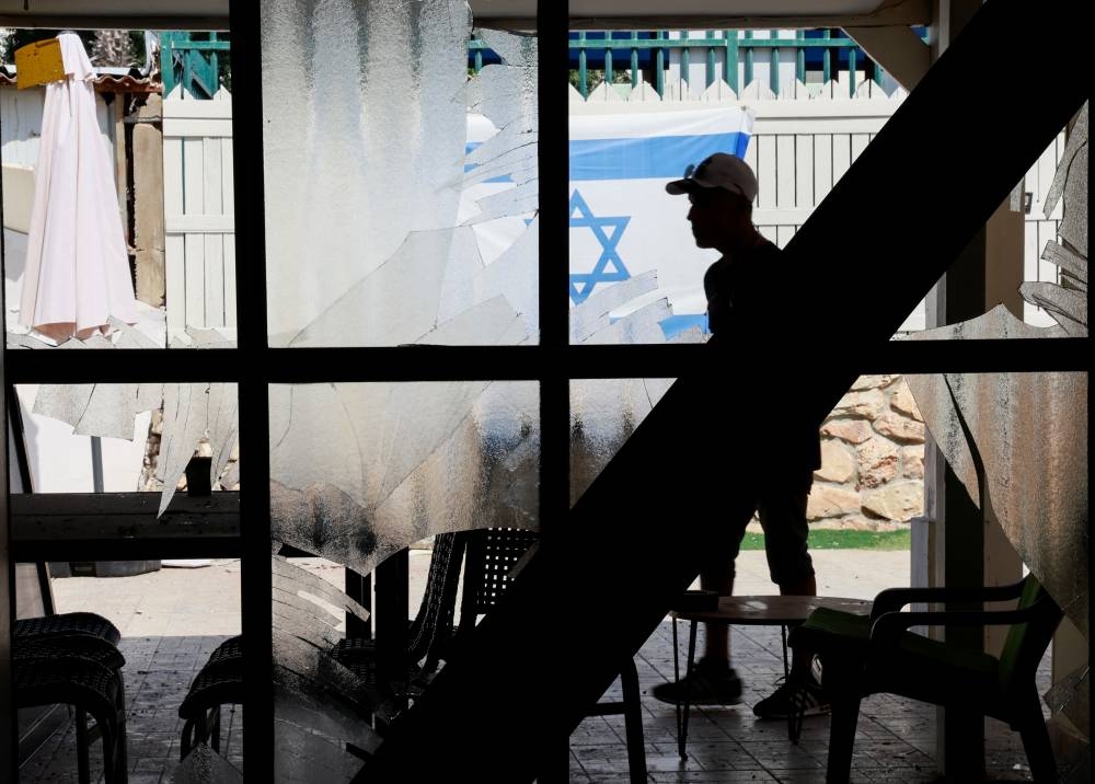 A person walks near broken windows of a damaged residential building after Hezbollah launched hundreds of rockets and drones towards Israel, in Acre, northern Israel on Sunday. REUTERS
