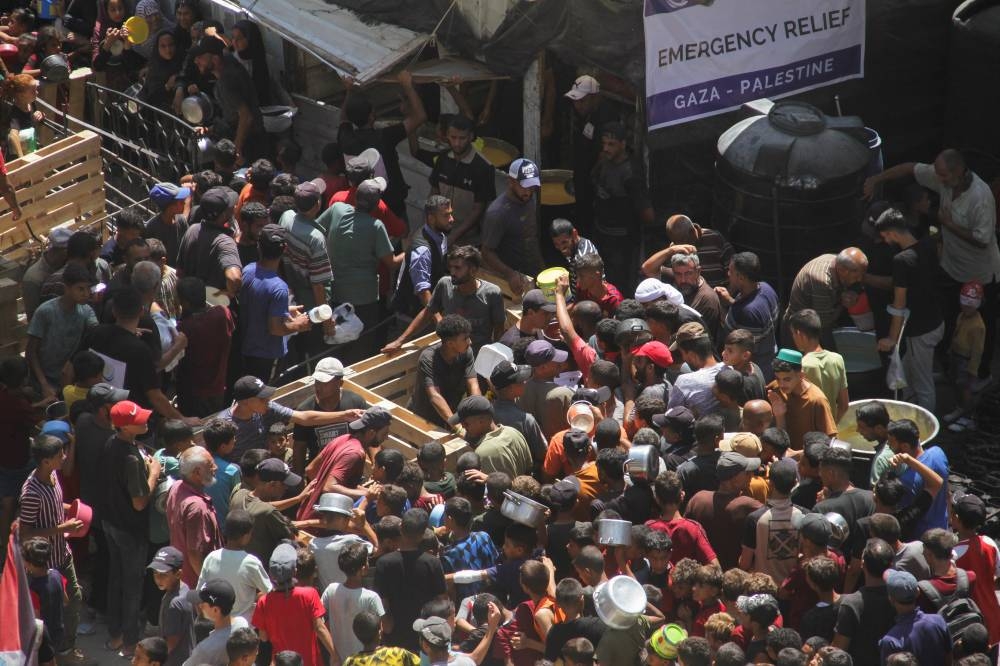 Palestinians gather to receive food cooked by a charity kitchen, near the ruins of houses destroyed during the Israeli offensive, in Jabalia in the northern Gaza Strip Monday. REUTERS