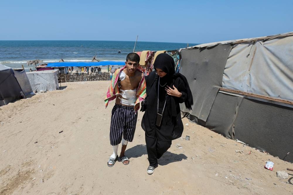Diaa Al-Adini walks with his sister Aya on a beach outside a field hospital, in Deir Al-Balah in the central Gaza Strip, on Tuesday. REUTERS