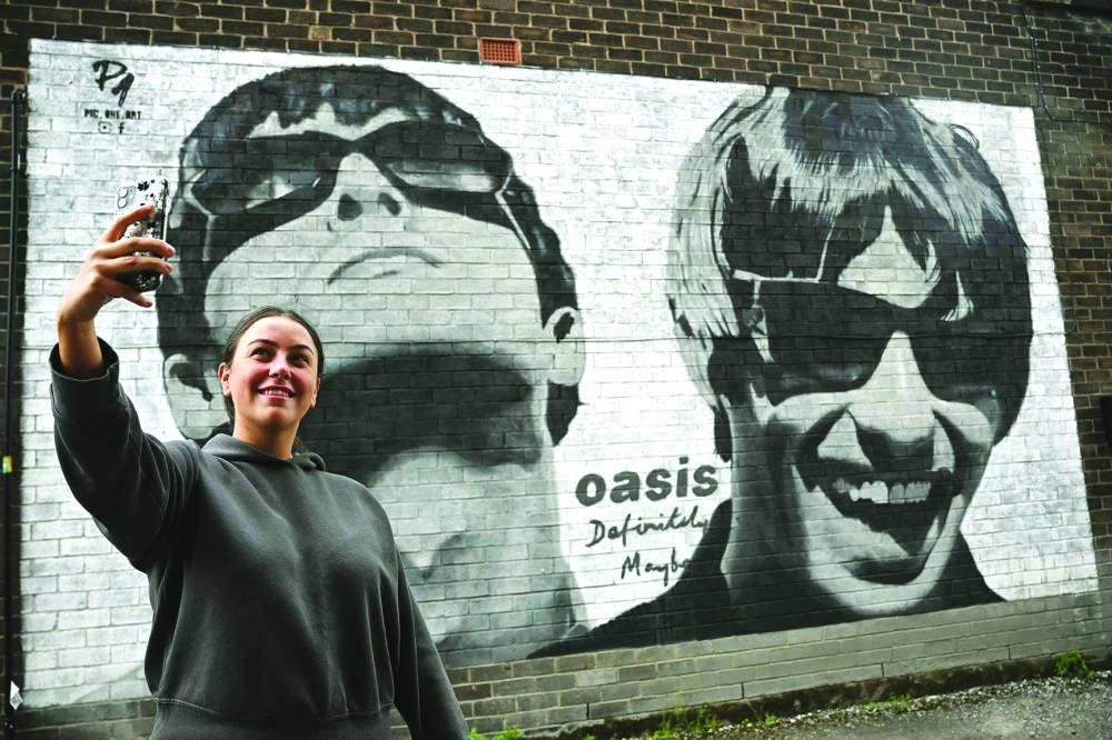 
Fan Emily McShane, takes a photograph of a new street artwork depicting Oasis’ Liam and Noel Gallagher, created by Manchester-based street artist Pic.One.Art. on the side of the Sifters Record store in Burnage, a suburb of Manchester, northern England. 
