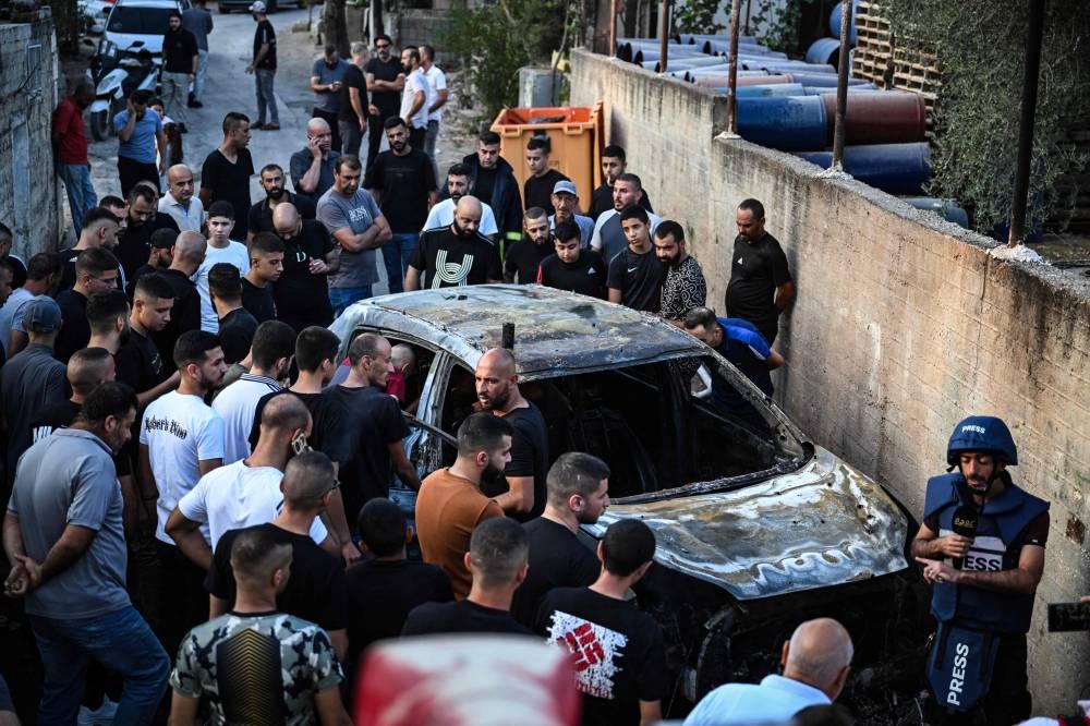 People surround a burnt car in the small town of Zababdeh, southeast of Jenin in the occupied West Bank on Friday, following an Israeli army raid.  AFP