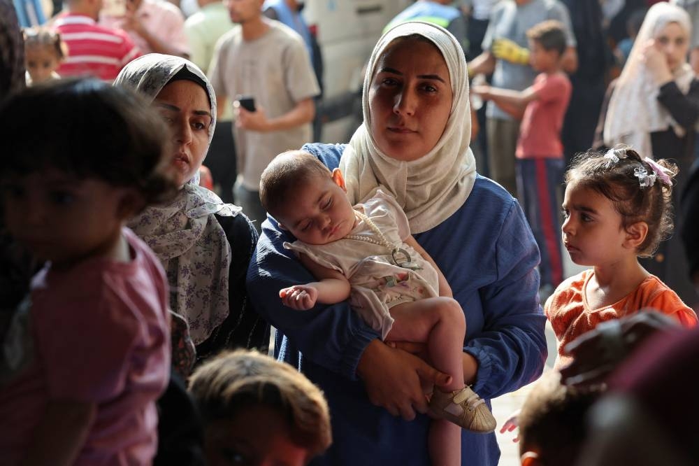 A displaced Palestinian mother, Wafaa Abdelhadi, carries her daughter Lynn as she waits to get her vaccinated against polio, in Deir Al-Balah, in the central Gaza Strip on Sunday.  REUTERS