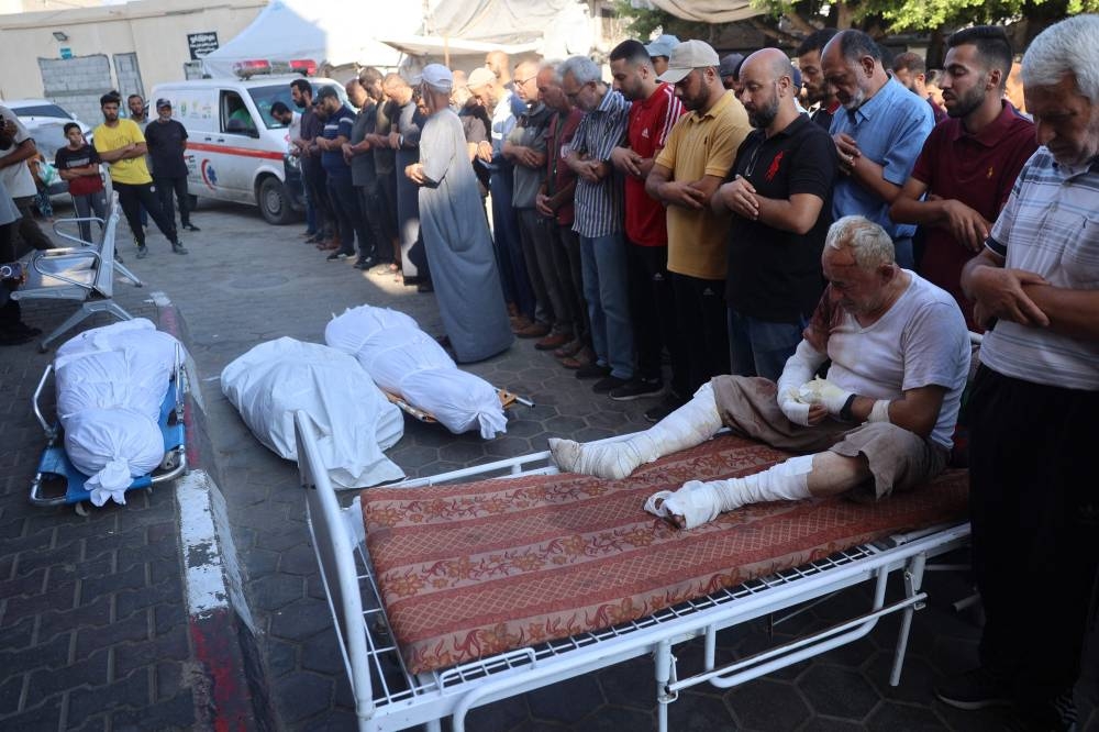 An injured Palestinian man mourns over the bodies of family members victims of Israeli bombardment, Saturday, in Deir el-Balah in the central Gaza Strip. AFP