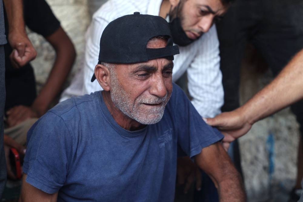 A Palestinian man is comforted as he mourns over the bodies of family members victims of Israeli bombardment, on Saturday, in Deir el-Balah in the central Gaza Strip. AFP
