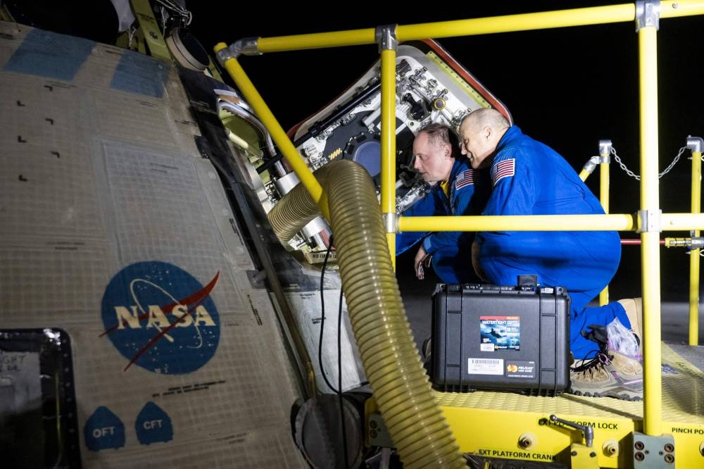 NASA astronauts Mike Fincke (L) and Scott Tingle looking inside NASA's Boeing Crew Flight Test Starliner spacecraft after it landed uncrewed at White Sands, New Mexico on Friday. AFP/NASA/Aubrey Gemignani