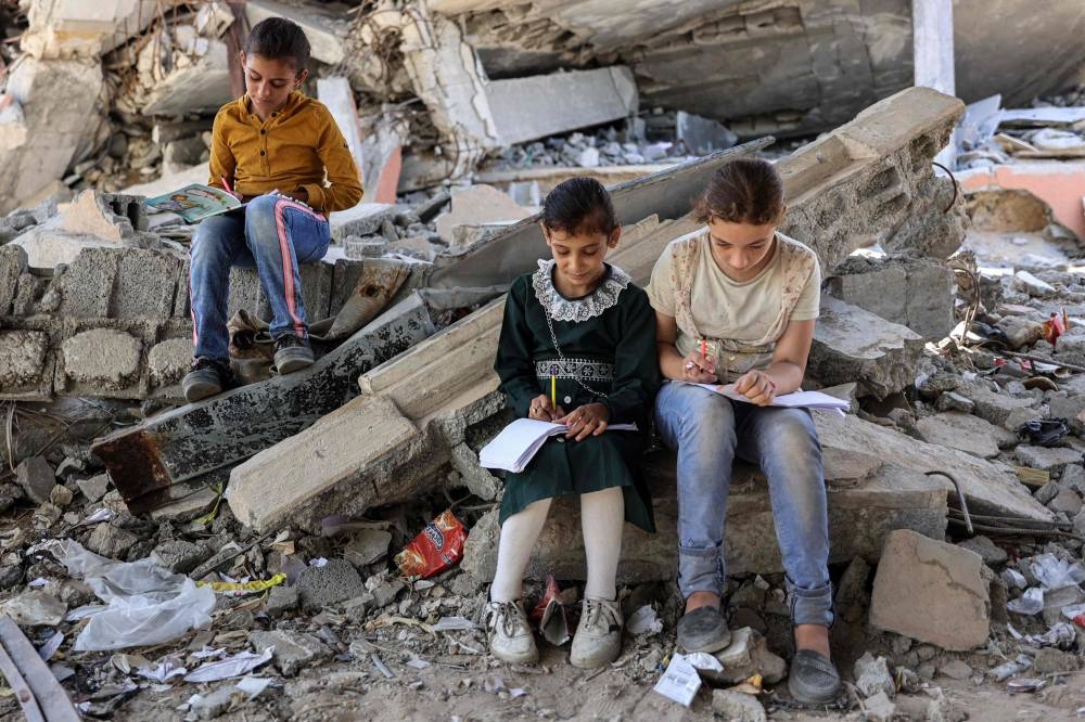 Children write in notebooks by the rubble of destroyed buildings near a tent being used as a make-shift educational centre for primary education students in Jabalia in the northern Gaza Strip on Sunday. AFP