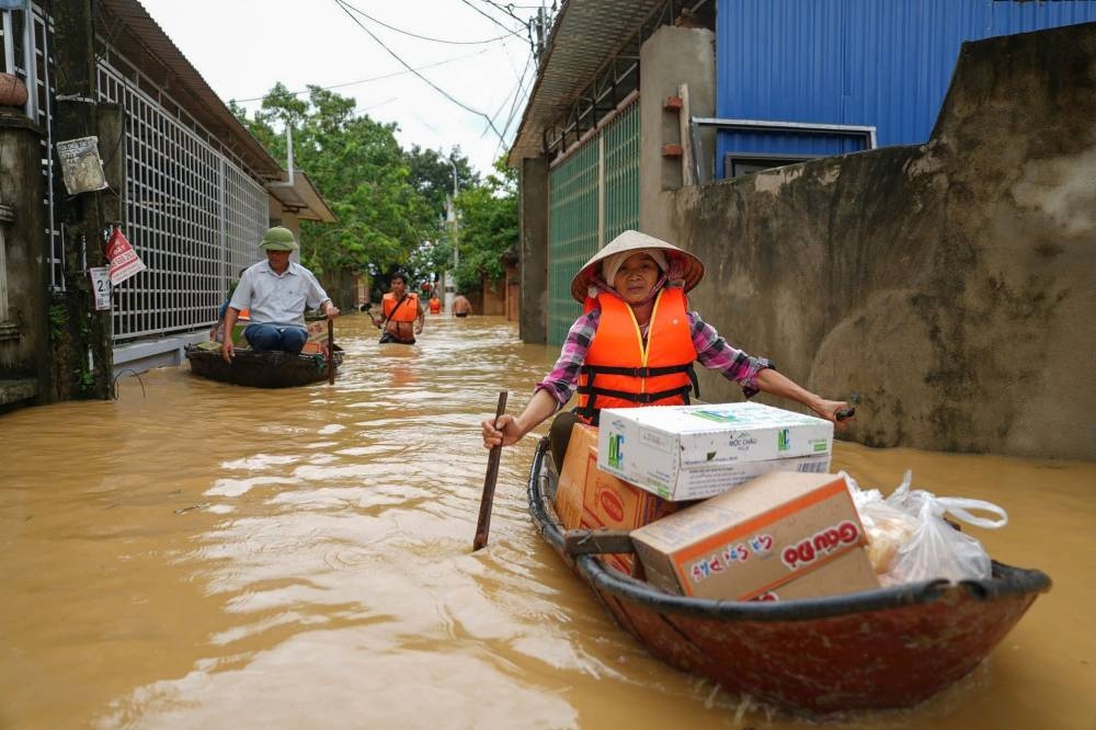 A woman rows a boat along a flooded street carrying packages of food in Thai Nguyen province on Tuesday. AFP