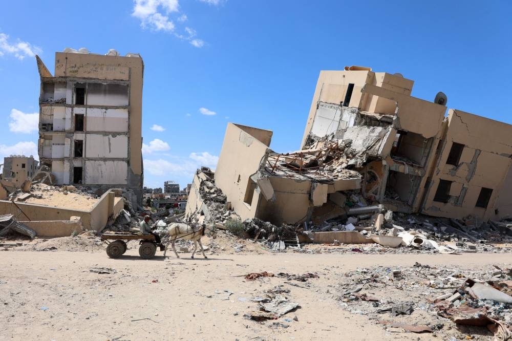 A Palestinian man rides a donkey-pulled cart in front of buildings heavily damaged in Israeli bombing, in Beit Lahia in the northern Gaza Strip on Saturday. AFP