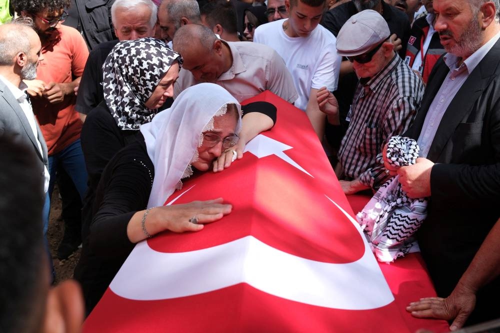 A relative of Aysenur Ezgi Eygi, mourns over her Turkish flag-draped coffin during the funeral ceremony at a cemetery in Didim, Turkiye.