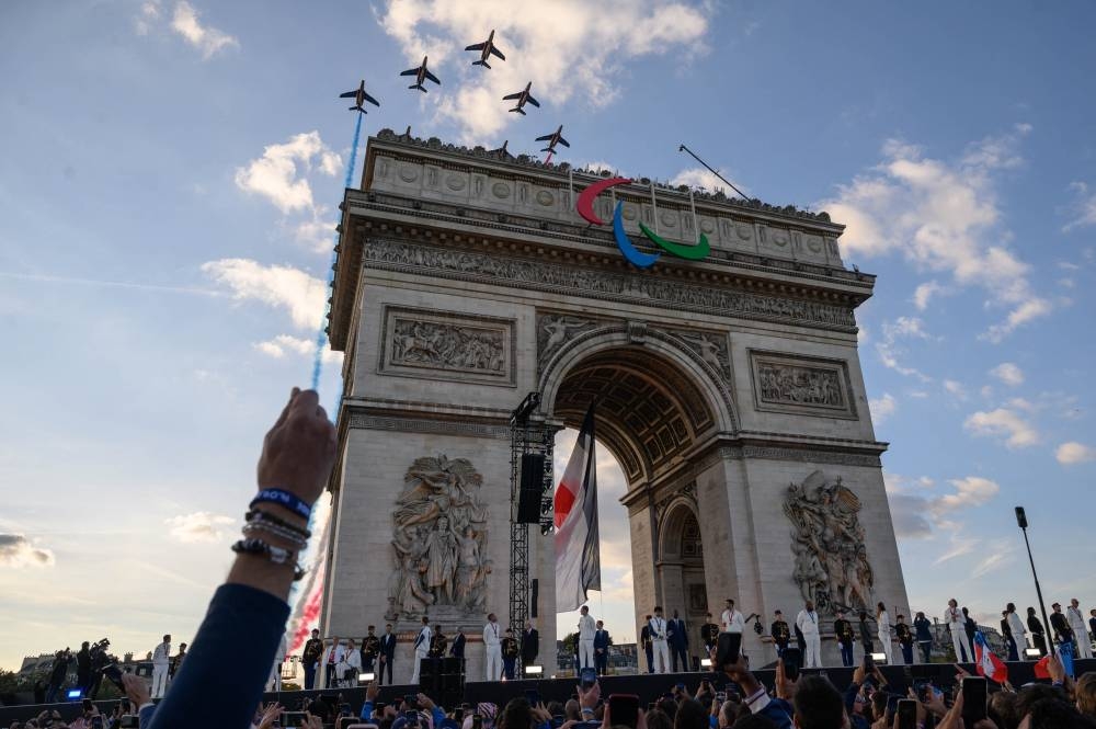 French Air Force Elite acrobatic flying team "Patrouille de France" performs over the Arc de Triomphe as French athletes who competed in the Paris 2024 Olympic and Paralympic Games appear on stage at the end of their parade on the Champs-Elysees avenue in Paris on Saturday. AFP