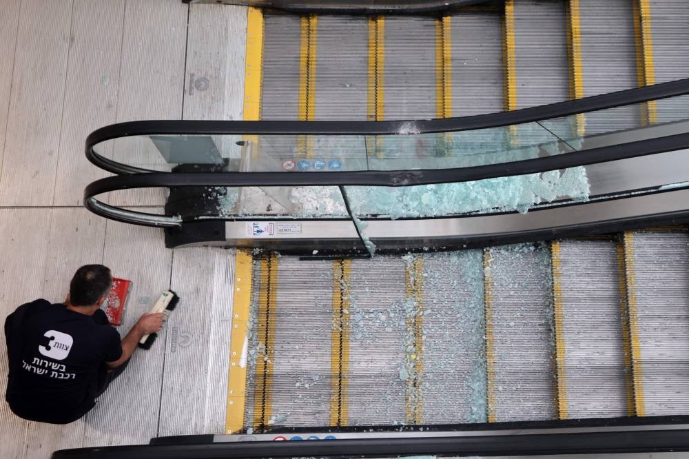 An employee sweeps shards of glass from an escalator damaged from the impact of a missile fired from Yemen, inside a train station in the Israeli town of Modin on Sunday. AFP