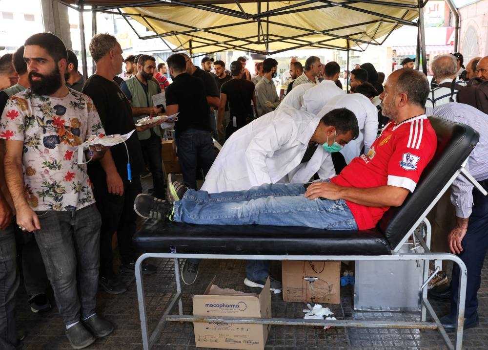 People gather as a man donates blood, following pager detonations across Lebanon on Tuesday, in Beirut suburbs, Lebanon on Wednesday. REUTERS