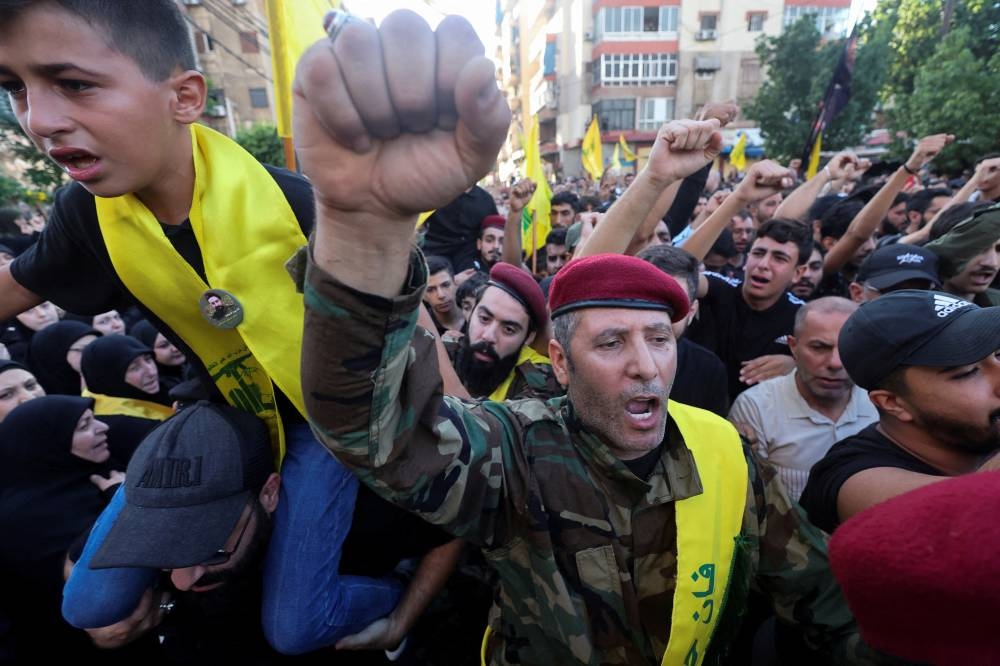 Hezbollah members raise their fists on the day of the funeral of three Hezbollah members, who were killed on Friday in an Israeli strike on Beirut's southern suburbs, Lebanon on Saturday. REUTERS