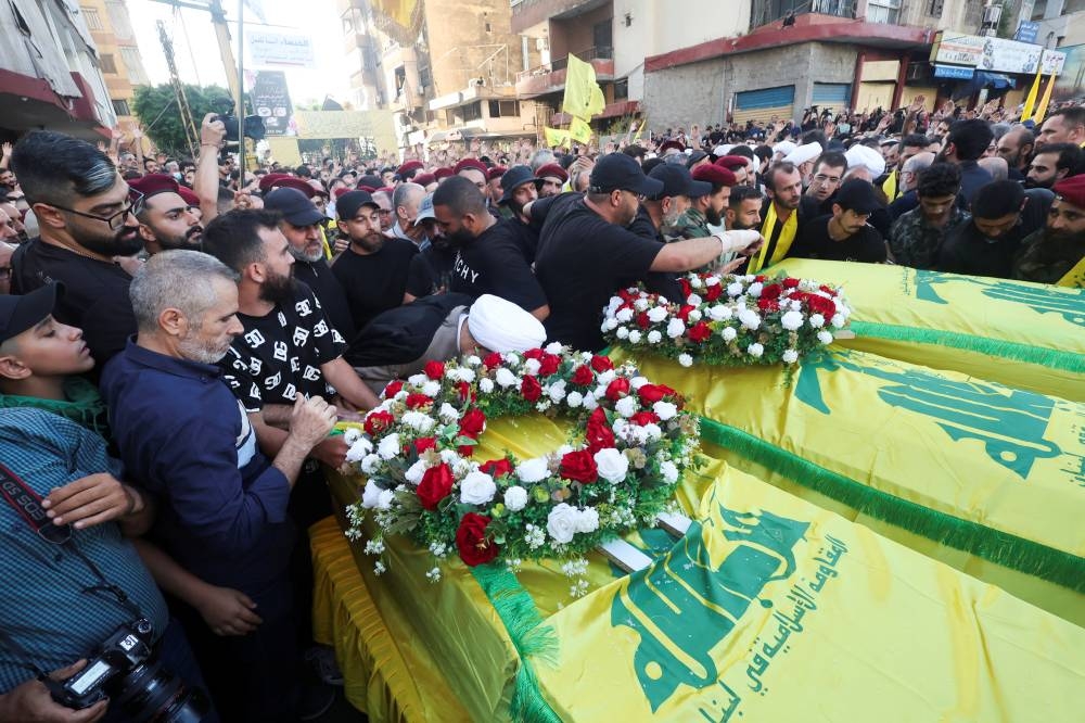 People stand next to coffins during a funeral of three Hezbollah members Hassan Youssef Abdel Sater, Ahmed Samir Deeb and Abbas Sami Muselmani, who were killed on Friday in Israeli strike on Beirut's southern suburbs, Lebanon on Saturday. REUTERS