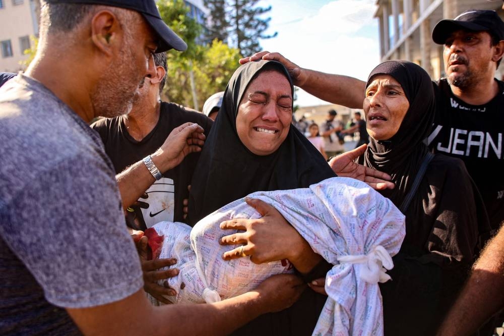 A woman mourns as she holds the shrouded body of her child who was killed during an Israeli strike on a school housing displaced Palestinians in Gaza City's Zaytoun neighbourhood, on Saturday. AFP
