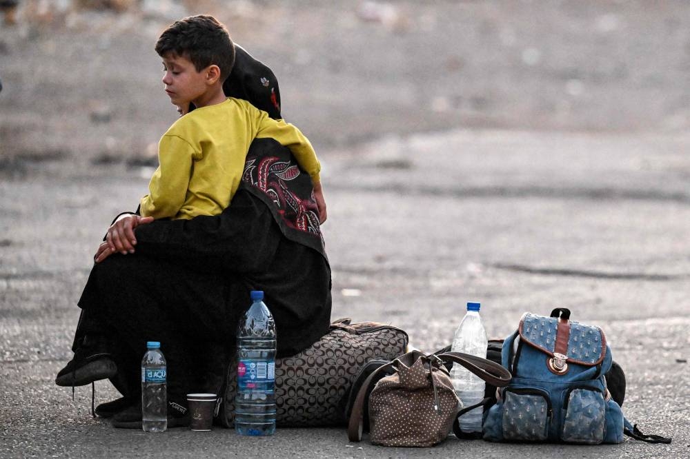 A woman sits with a child on her lap next to bags on the ground as people fleeing from Lebanon arrive on the Syrian side of the border with Lebanon in Jdeidat Yabus in southwestern Syria on Tuesday. AFP