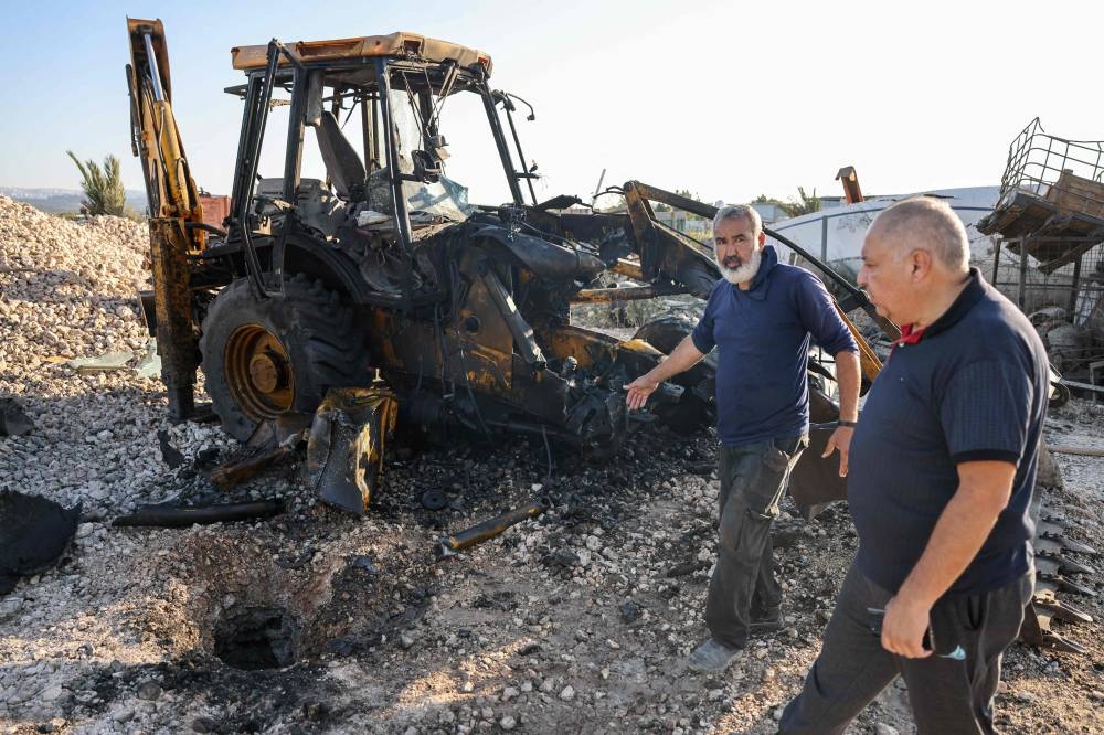 Men walk past a hole in the ground and a burnt tractor after a rocket fired from southern Lebanon hit the town of Kfar Manda in northern Israel on Tuesday. AFP