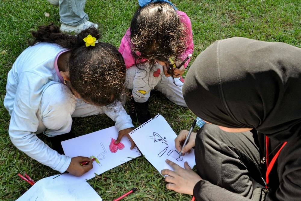 A woman draws with children while sitting on a lawn at a public park as people displaced by conflict from southern Lebanon wait to be relocated to a temporary reception shelter in the northern city of Tripoli on Wednesday. AFP