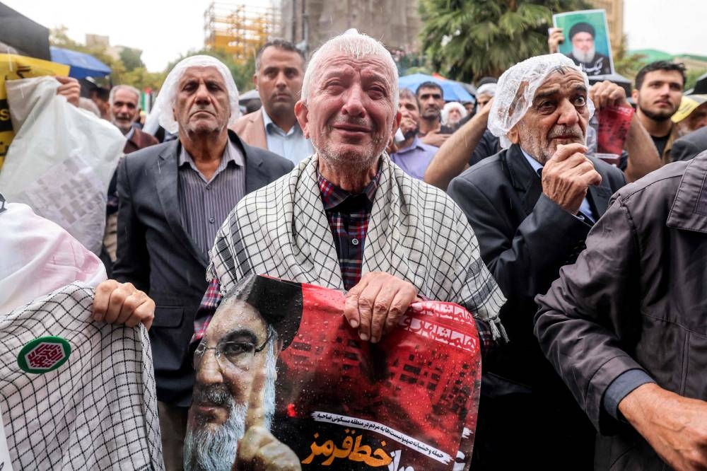 A man reacts as he holds a poster reading "crossing a red line" in Persian next to an image of Hassan Nasrallah, the late leader of the Lebanese Hezbollah group, during an anti-Israel protest in Tehran's Palestine Square on Saturday. AFP