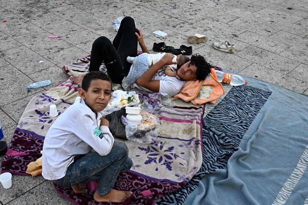 A young man and children who fled Israeli bombardment on Beirut's southern suburbs, gather in the Lebanese capital's seaside corniche where they spent the night, on Saturday. AFP