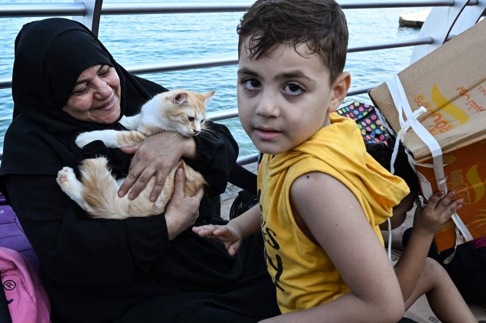 A woman who fled Israeli bombardment on Beirut's southern suburbs, holds a cat along the Lebanese capital's seaside corniche where she spent the night with her family, on Saturday. AFP