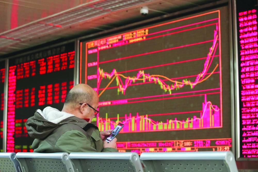 An investor looks at his mobile phone in front of a board showing stock information at a brokerage office in Beijing