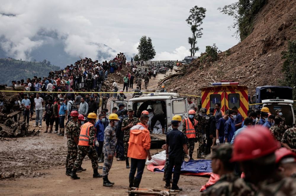 People stranded at the Tribhuwan Highway gather as rescue personnel put the bodies retrieved from the landslide triggered by heavy rainfall into an ambulance in Dhading, Nepal, on Sunday. REUTERS