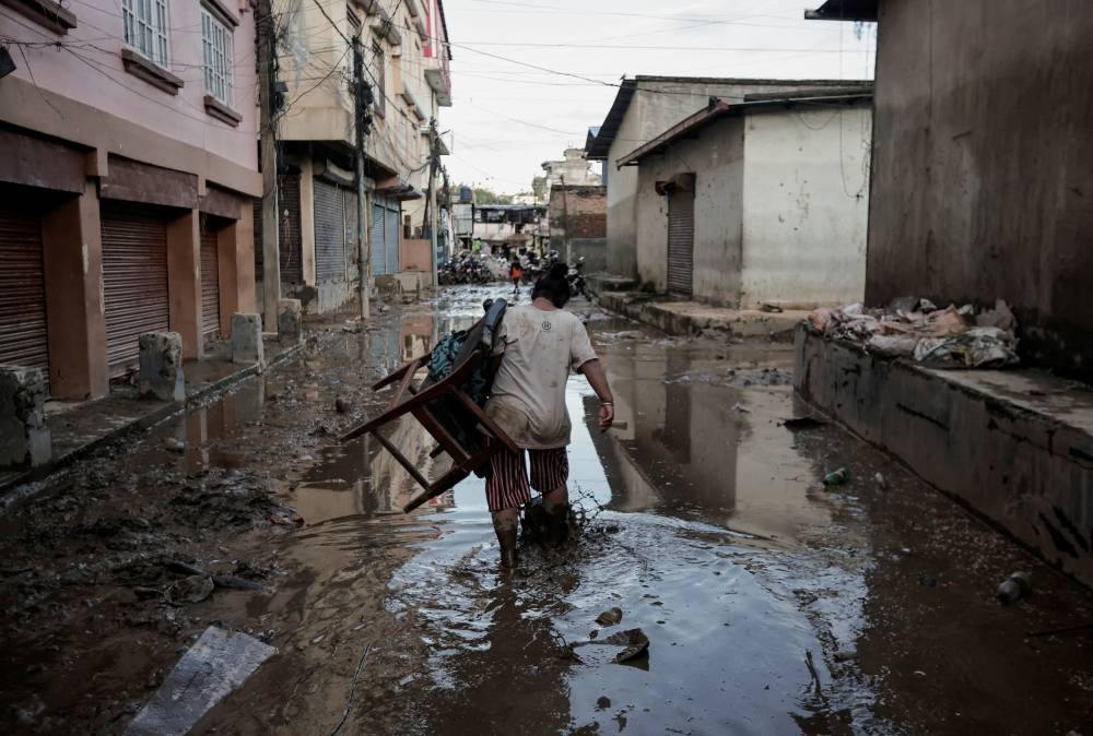 A woman carrying a chair walks along a muddy street as the floodwater recedes from a residential area that was flooded by the overflowing Bagmati River following heavy rains in Kathmandu, Nepal, on Sunday. REUTERS
