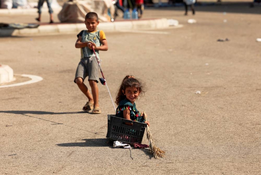 A boy pulls a girl in a basket at a parking lot where Syrian refugees, who fled from southern Lebanon villages due to ongoing hostilities between Hezbollah and Israeli forces, are taking shelter, in Sidon, Lebanon on Monday. REUTERS
