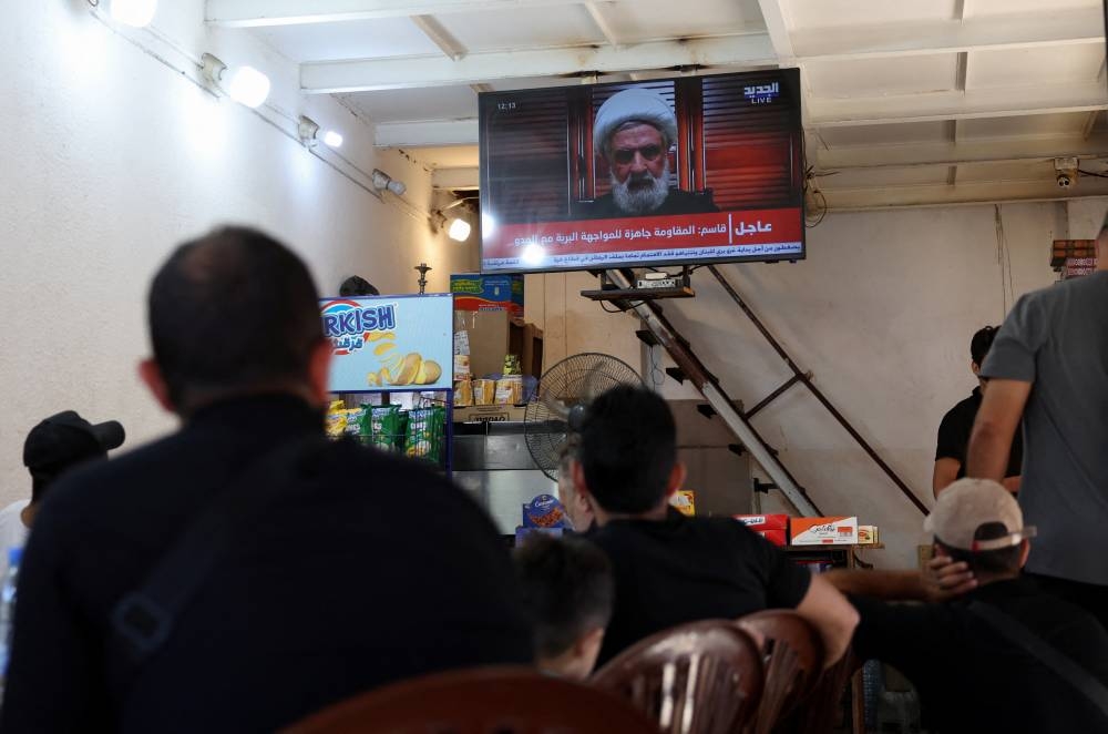 People watch Hezbollah deputy leader Sheikh Naim Qassem delivering a televised address, as they sit at a cafe in Beirut, Lebanon, on Monday. REUTERS