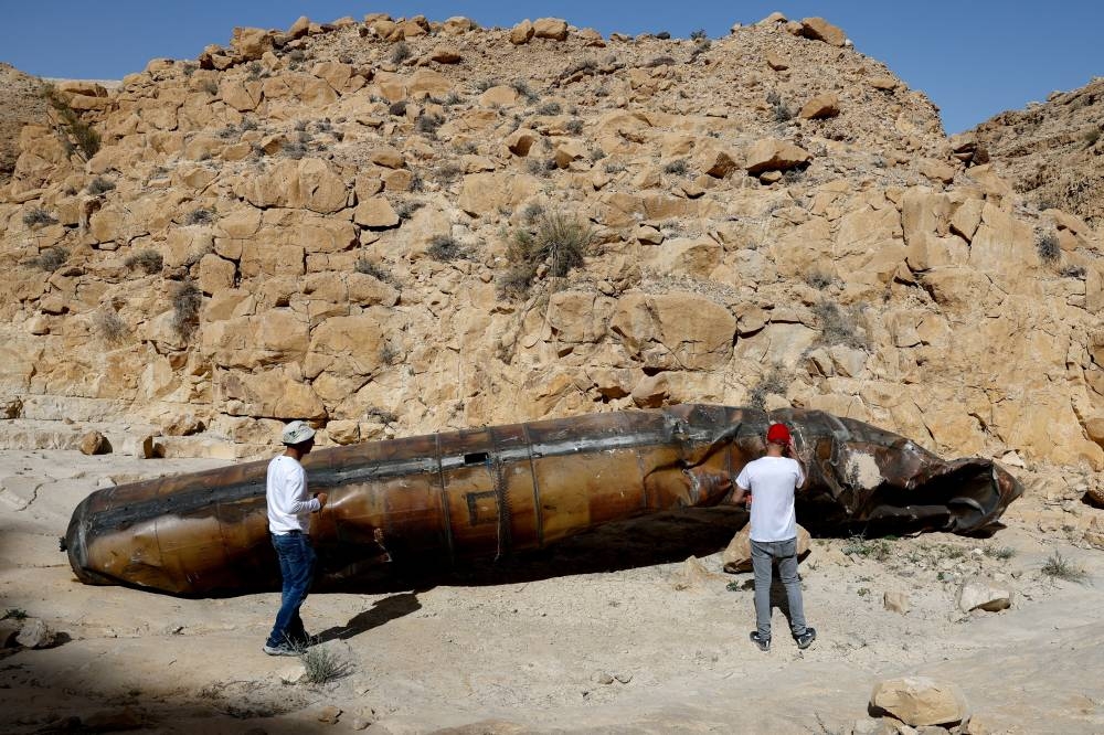 Members of military personnel in civilian clothing inspect apparent remains of a ballistic missile lying in the desert, following a massive missile and drone attack by Iran on Israel, near the southern city of Arad, Israel April 24, 2024. REUTERS