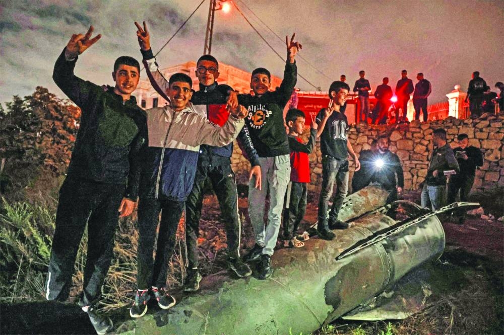 Palestinian youths celebrate as they stand atop a fallen projectile after Iran launched a barrage of missiles at Israel, in the city of Ramallah in the occupied West Bank Tuesday.