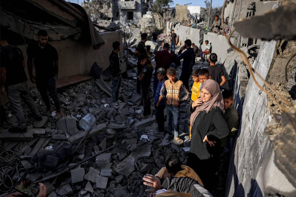 A woman looks on as she stands with children while Palestinian Civil Defence rescuers extract the body of a victim from underneath the rubble of a collapsed building in Khan Yunis in the southern Gaza Strip on Wednesday. AFP