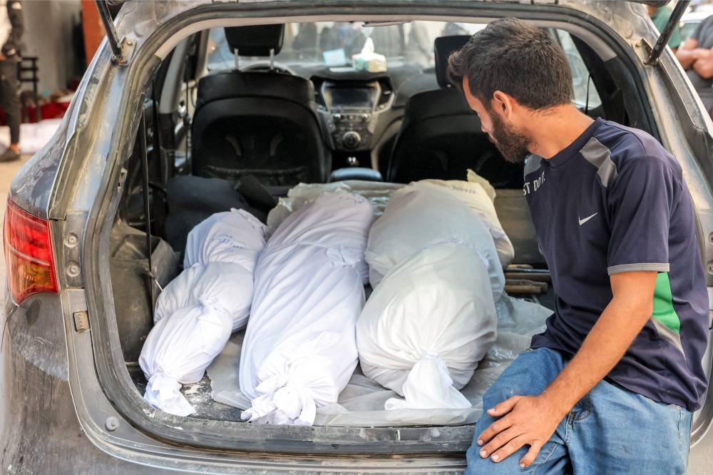 A man sits in the back of a vehicle with the shrouded bodies of victims killed in overnight Israeli bombardment after they were taken to the Ahli Arab hospital in Gaza City on Wednesday. AFP