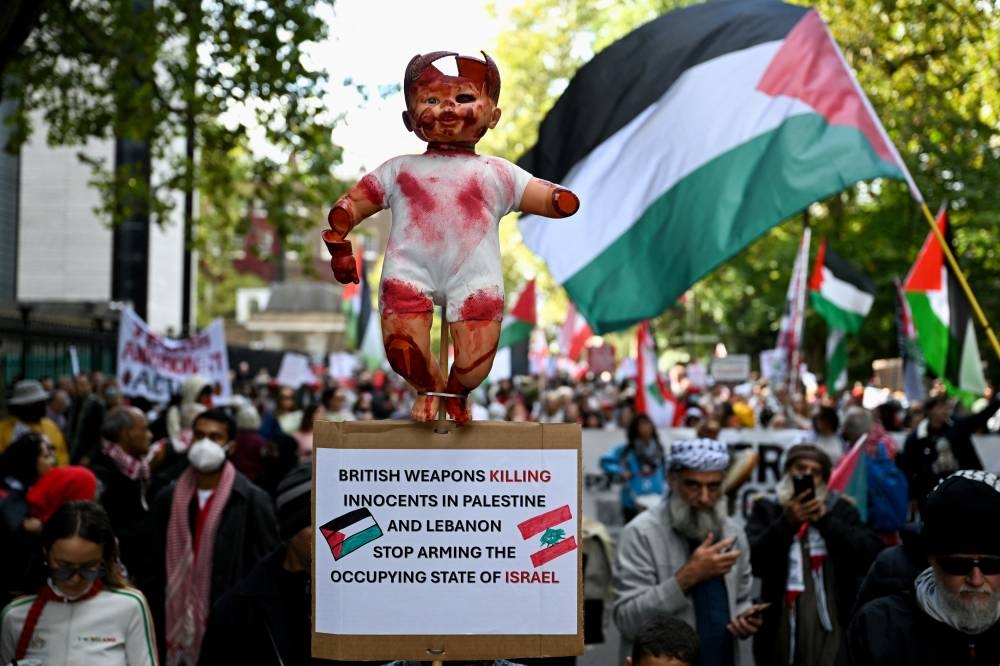 A protester holds a sign with a broken baby doll as a Palestinian flag is waved behind during a demonstration in support of Palestinians in Gaza, ahead of the October 7 attack anniversary, in London, on Saturday. REUTERS