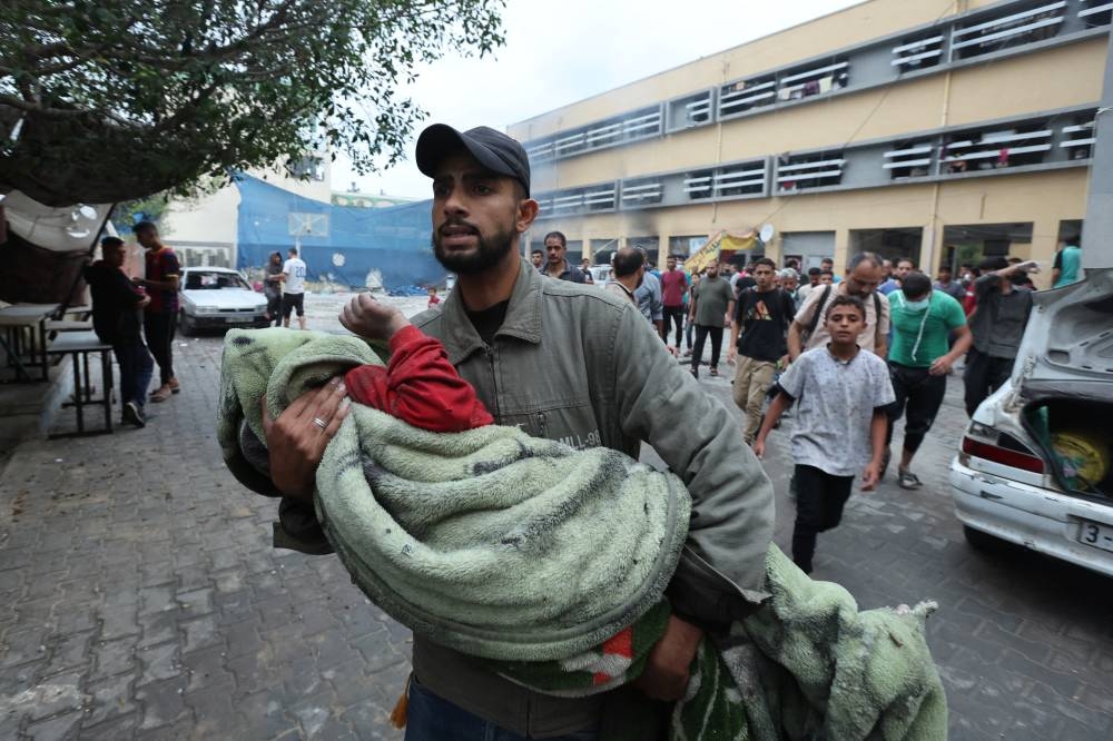 A man carries a Palestinian boy killed in an Israeli strike on a school sheltering displaced people in Deir Al-Balah, in the central Gaza Strip, on Sunday. REUTERS