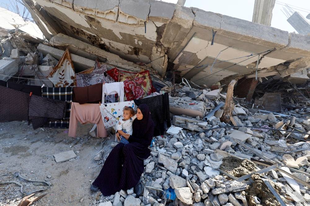 A Palestinian woman sits with a child next to rubble of a house destroyed in Israel's military offensive, in Khan Younis in the southern Gaza Strip, on Monday. REUTERS