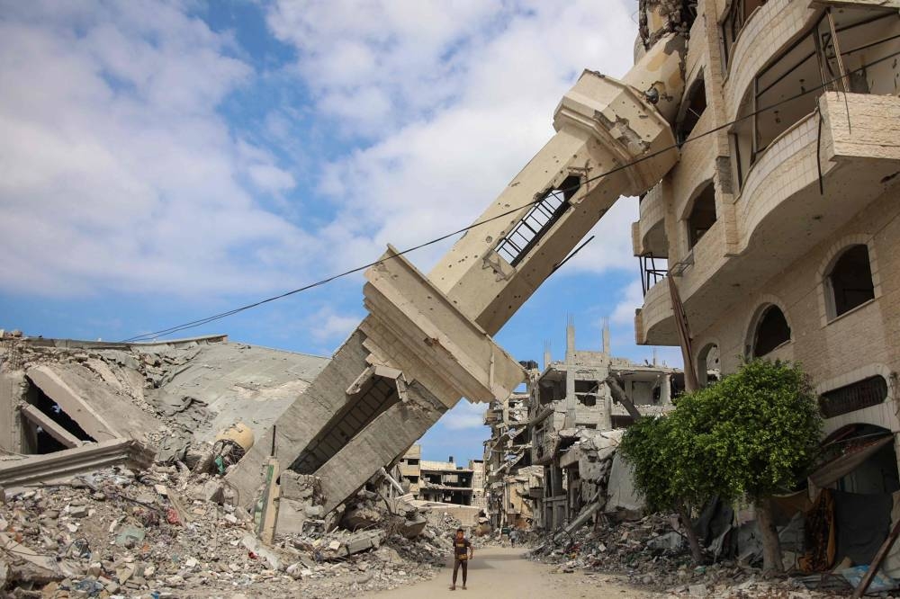 Palestinians walk beneath the tilted minaret of a destroyed mosque in the Shujaiya neighbourhood of Gaza City on Monday. AFP